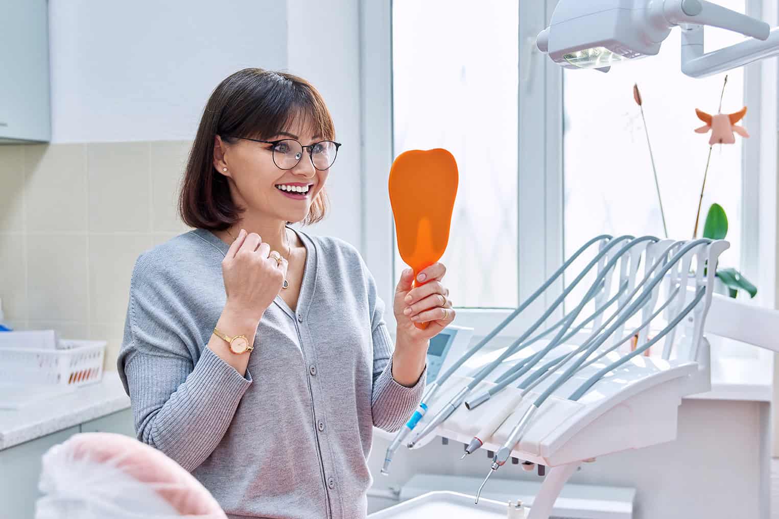 Happy woman dentist patient with a mirror in her hands looking at her teeth